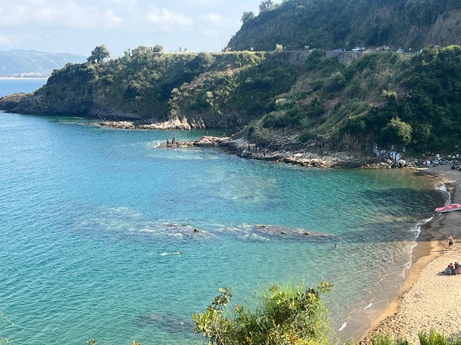 Plage ensoleillée avec eau claire et paysages côtiers verdoyants.